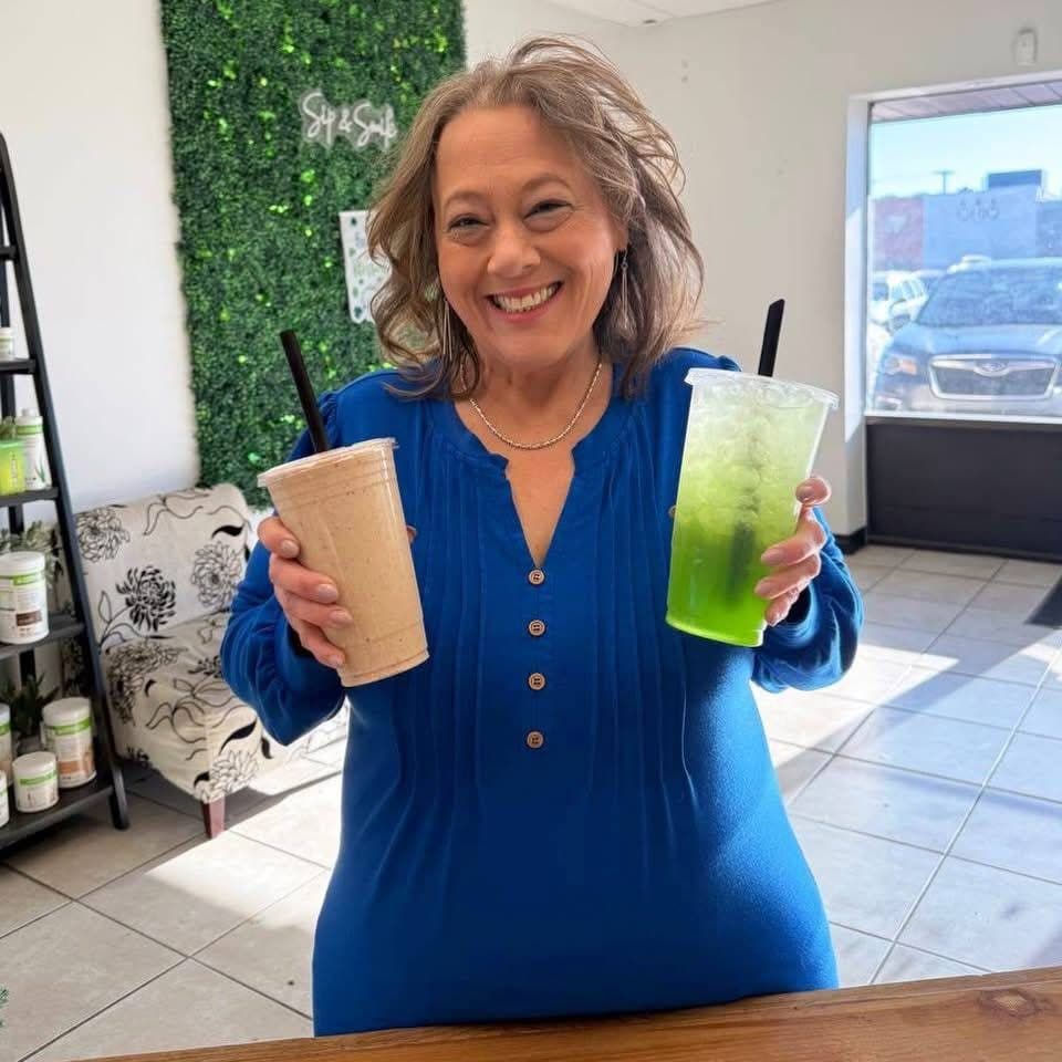 A smiling guest holding a protein shake and a green loaded tea at the NutriToledo counter